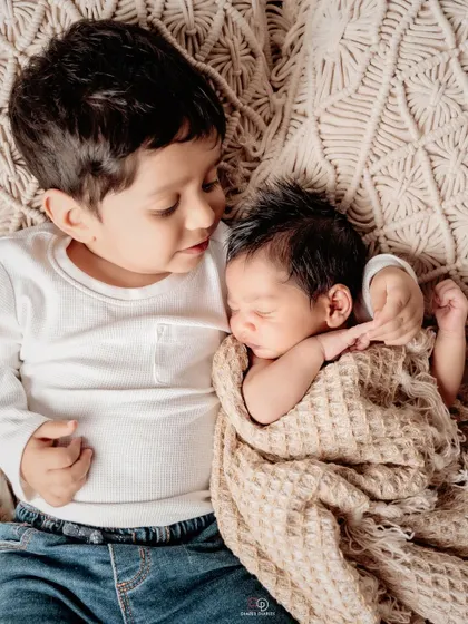 A tender moment between two brothers. The older brother lies down and gently holds his newborn baby brother, showcasing the beginning of a lifelong bond.