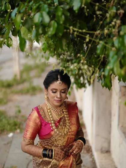 A quiet moment before the ceremony begins. This bride's makeup features a beautiful pink eyeshadow and matching lip, complementing her vibrant pink and gold Kanchipuram silk saree.