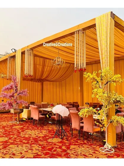 A guest seating area within the large yellow tent. The decor is consistent, with yellow drapes and elegant table setups.