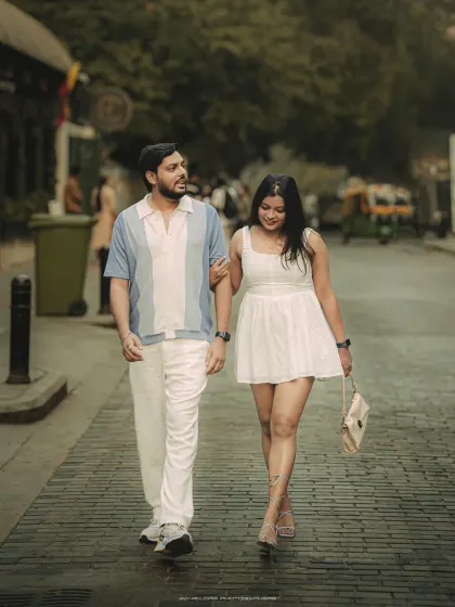 Another angle of the couple's city stroll, this shot captures their interaction and confident style as they walk through a chic urban lane.