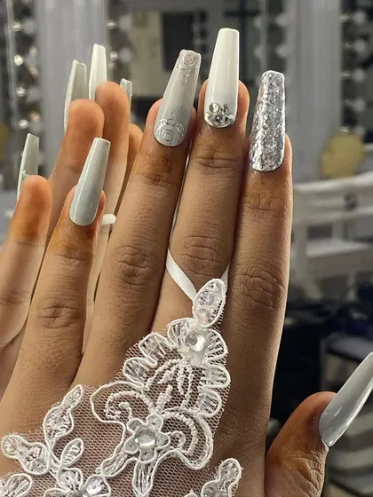 An elegant and intricate set for a white wedding theme. It features long, square-shaped nails with white 3D floral details, silver glitter, and delicate crystal accents.