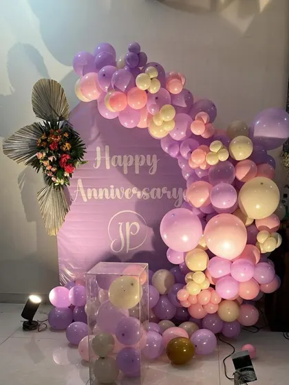 Another view of the purple-themed anniversary decor. The arrangement includes a clear plinth filled with balloons and a floral accent, adding layers of detail to the design.