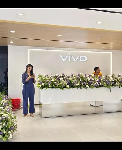 The main reception desk at a VIVO store, adorned with flowers for the opening. The minimalist design with backlighting and clean lines creates a strong brand statement right at the entrance.