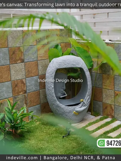 A tranquil corner of a backyard featuring a unique water feature with a face sculpture. The earthy tones of the tiled wall and the green grass create a natural and calming setting.