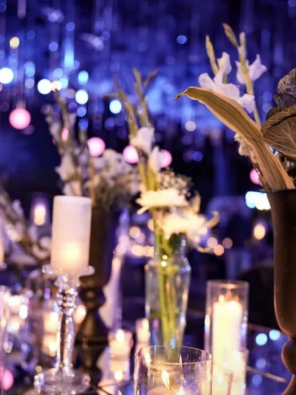 A close-up of a candlelit tablescape at a glamorous evening reception. The candlelight reflects beautifully against the dark, moody lighting.