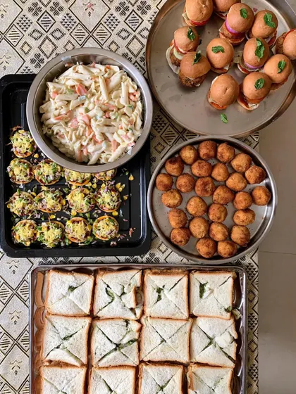 A beautiful spread of party food, including Mini Burgers, White Sauce Pasta Salad, Mini Pizzas, and Chutney Sandwiches.