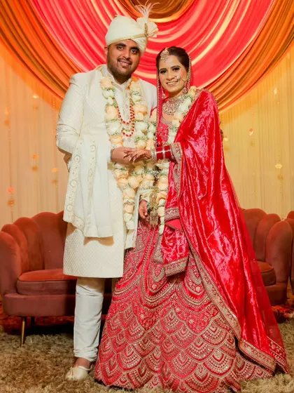 A lovely portrait of the bride and groom on their wedding day. They are holding hands, dressed in beautiful red and white outfits, ready to start their life together.