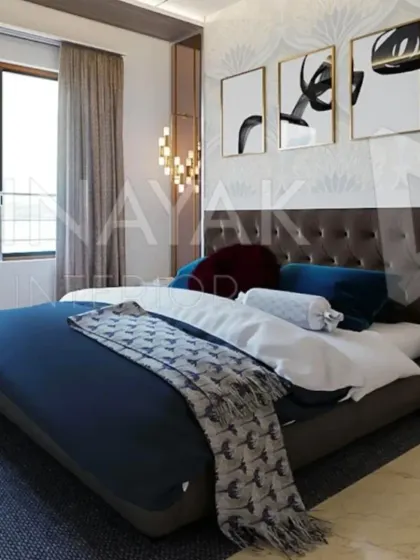 Natural light floods this bedroom, highlighting the abstract artwork and the subtle texture of the wallpaper. The combination of a dark tufted headboard and deep blue bedding creates a sophisticated and restful mood.