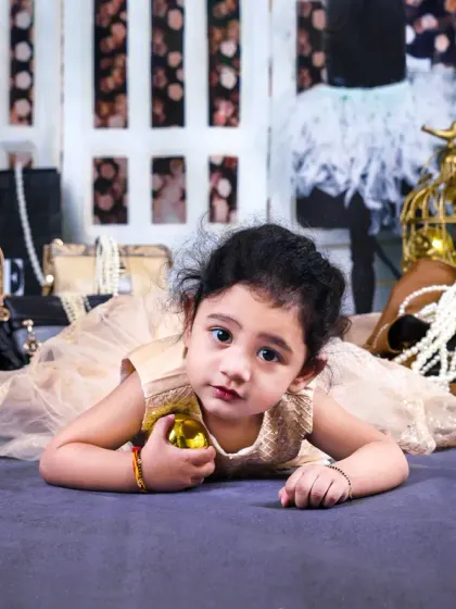 Lying on her tummy, this baby girl looks at the camera with big, expressive eyes amidst a high-fashion-themed set.