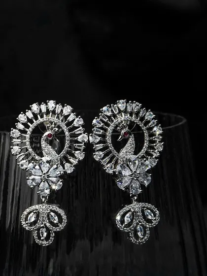 Peacock-inspired earrings shot with dramatic lighting against a dark glass. This creative approach makes the product look dynamic and luxurious.