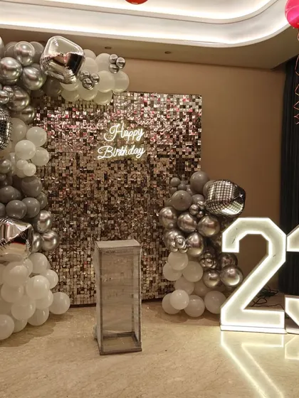 A stylish 23rd birthday with a silver shimmer wall and marquee numbers. The grey, white, and chrome balloon arch adds a modern and chic touch.
