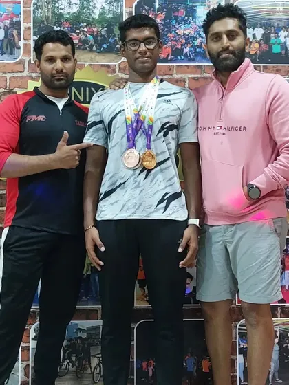 The team stands proud with our champion athlete. Our gym's photo wall in the background is filled with memories of our community's achievements, and we are thrilled to add Nithik's success to it.