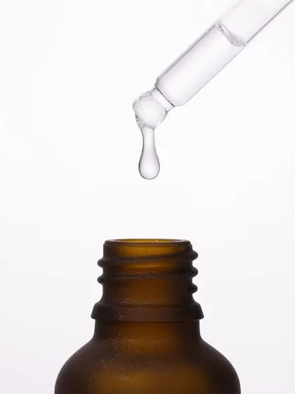 We captured the precise moment a single drop of serum falls from the dropper. This macro shot, set against a pure white background, emphasizes purity, potency, and the scientific precision behind the formula.