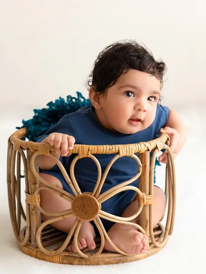 A full view of the baby sitting happily in a flower-shaped wicker basket prop.