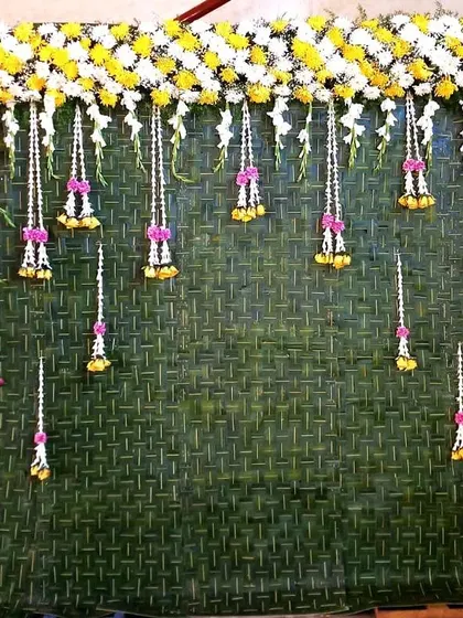 A simple yet elegant backdrop design. We used a woven mat of coconut leaves and decorated it with a border of yellow and white chrysanthemums and delicate hanging floral tassels for a fresh, festive look.