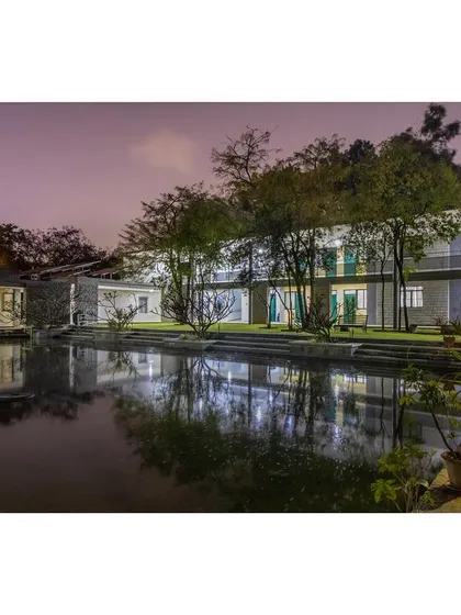 A night view of the new ward block, with the water reflecting the lights and the surrounding trees.