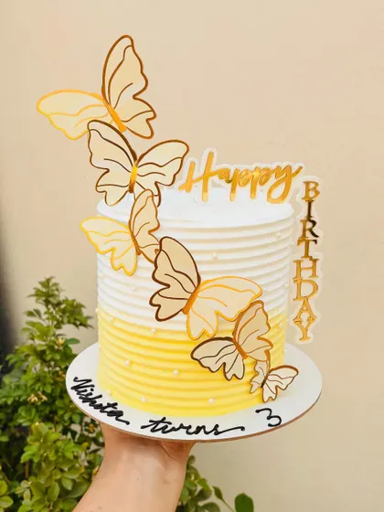 A sunny yellow ombre cake with cascading butterfly toppers. This is a cheerful and elegant design for a third birthday.