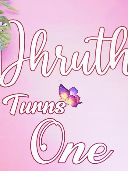 A close-up of a custom backdrop for a first birthday. The 'Dhruthi Turns One' text is designed in elegant script, perfectly matching the pink butterfly theme.