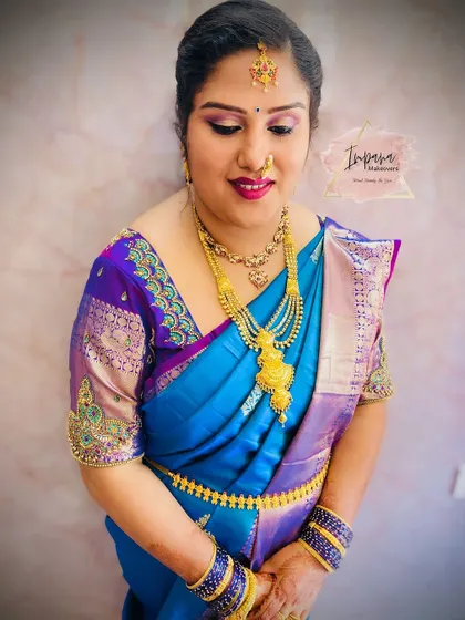 A guest looking lovely in a blue and purple silk saree for a housewarming. The makeup is bright and festive.