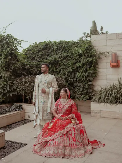 A regal portrait with the bride seated and the groom standing beside her, exuding elegance.