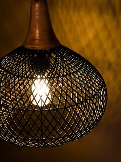 A close-up view of the lit black pendant. The light from within highlights the diamond-shaped pattern of the weave, creating a captivating visual effect against the dark finish.