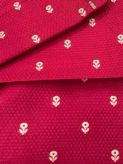 This bright pink Banarasi brocade fabric is woven with small butis and a silver zari border, making it a perfect choice for a traditional saree or a festive suit.