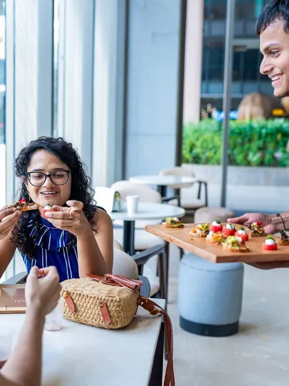 A server presenting a tray of canapés to a smiling customer at our RMZ Ecoworld location. We love to delight our guests.