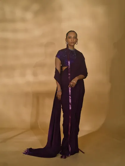 A classic lookbook shot from the 'Amethyst Edit'. The simple, standing pose provides a clear and unobstructed view of the purple draped saree, perfect for a designer's catalogue.