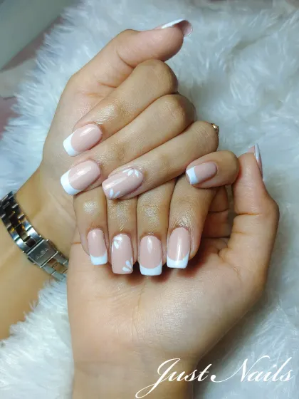 A soft and subtle French manicure on shorter, square-shaped nails. The accent nails feature a delicate, hand-painted white floral design, perfect for a minimalist bride.