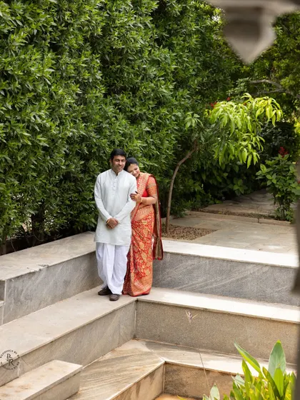 A candid shot of a couple in a lush green garden during a family function, capturing a quiet moment together.