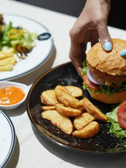 A close-up of someone enjoying my signature burger, served with a side of crispy potato wedges.