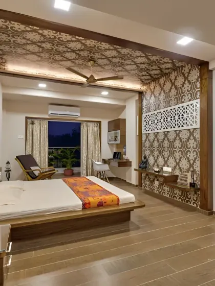 A spacious master bedroom with an integrated wooden bed frame and a long, wall-mounted unit that serves as both a desk and a vanity area. The intricate ceiling and wall patterns add a touch of traditional elegance.