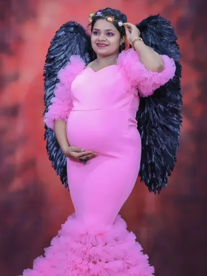 A creative maternity shoot with a woman in a pink mermaid-style gown, complete with black angel wings for a unique and artistic touch.