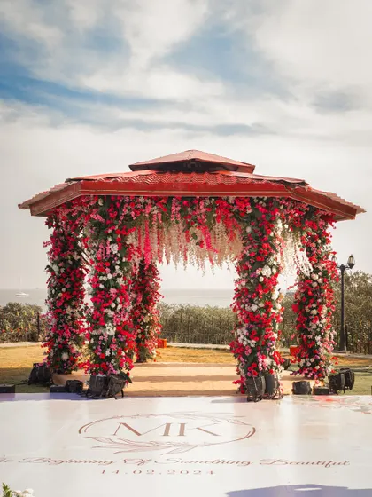 A stunning floral mandap set against the sea, designed for a celebrity wedding. The vibrant red flowers create a dramatic and romantic focal point.