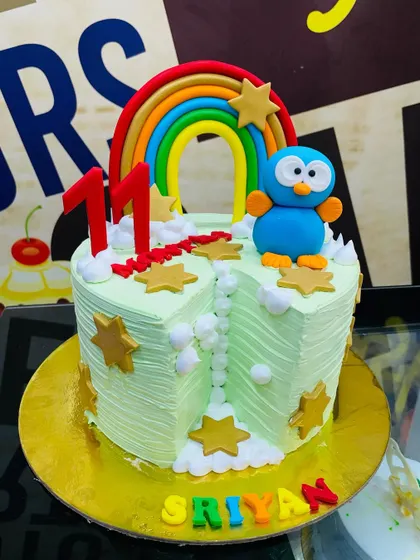 A 2kg heart-shaped cake with a rainbow, stars, and a cute blue bird character.