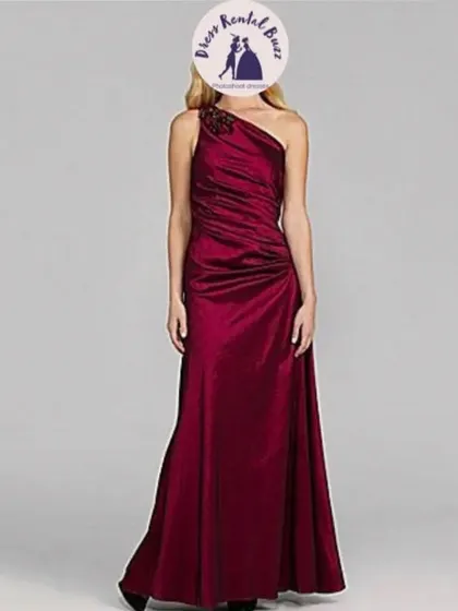This one shoulder satin gown in a wine red color features ruching and an embellishment on the strap.