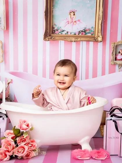 A baby girl enjoys a "spa day" in a glamorous pink-themed setup, complete with a miniature bathtub and shopping bags. This fun and sassy shoot is perfect for celebrating a little fashionista's personality.