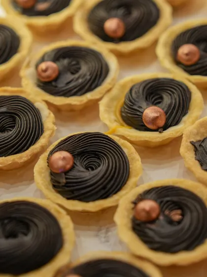 An array of our mini chocolate tarts, with a swirl of rich ganache and a single metallic chocolate pearl. The presentation is simple, elegant, and focuses on the quality of the chocolate.