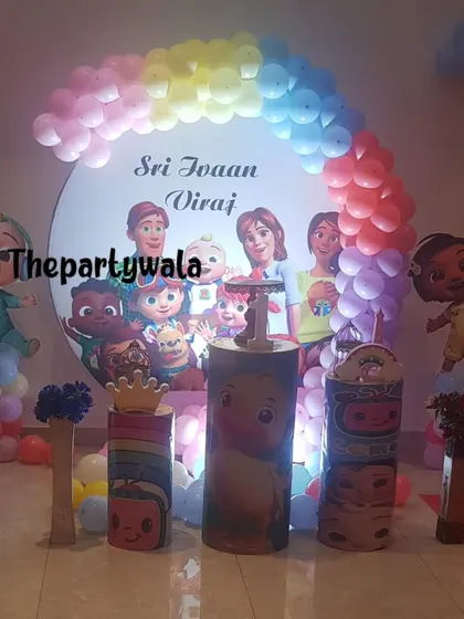 A Cocomelon party with a large character backdrop and themed pedestals.