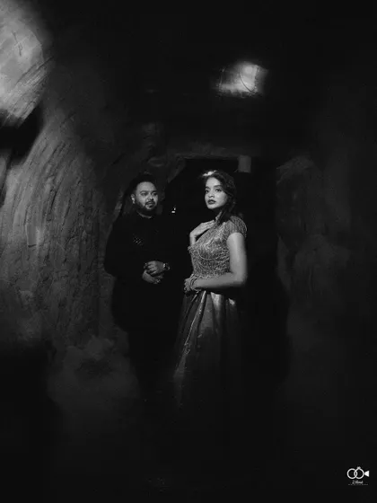 A moody and dramatic black and white portrait of a couple in a dark, cave-like setting, creating a mysterious and romantic image.