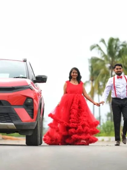 A modern, fun shot with a couple walking down a road. The woman is in a bright red ruffled gown, while the man sports a casual-formal look with suspenders and a bow tie.