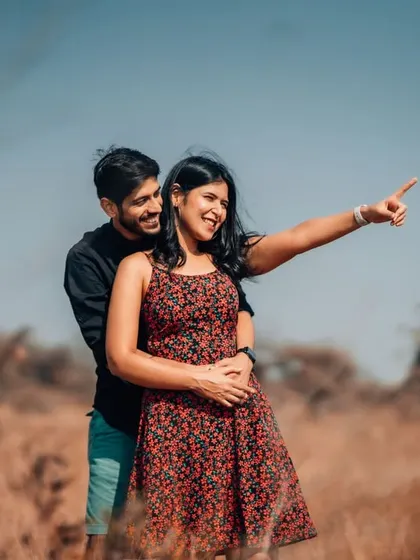 A joyful pre-wedding photo in an open field, with the groom-to-be lifting his partner as she points towards their future together.