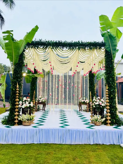 An eco-friendly mandap that is both beautiful and sustainable. The structure is built with lush green foliage and banana plants, complemented by a canopy and strings of delicate white jasmine flowers, creating a fresh, natural, and traditionally rooted aesthetic.