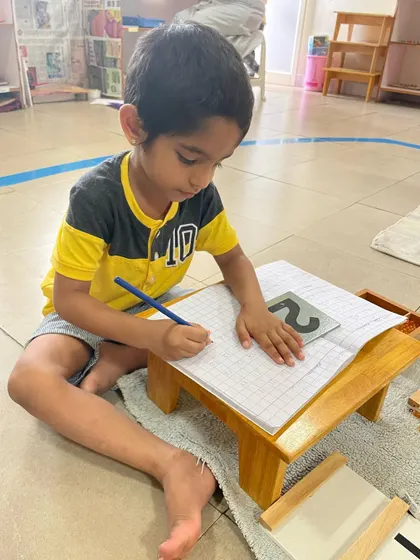 Using a sandpaper number as a guide, this child practices writing numerals. The tactile experience of tracing the rough number helps to create muscle memory, making the abstract shape of the number concrete.