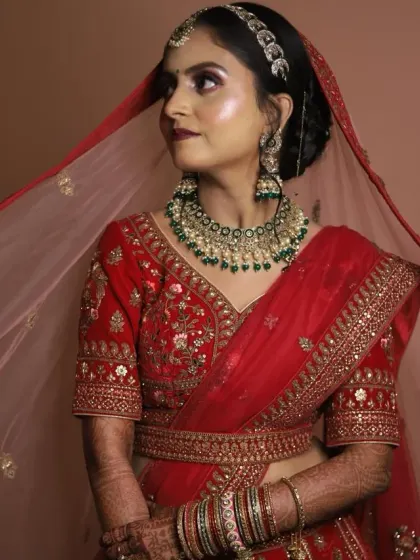 This bridal look features a beautiful red and green color combination. The hairstyle is a classic bun decorated with red roses and pearls, complementing her stunning lehenga.