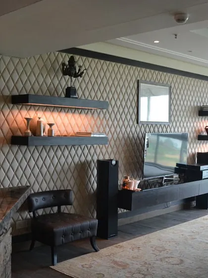 A view of the living and media room from the Magnolias project, showcasing a sophisticated and comfortable space. The design features a leather-paneled wall, custom shelving, and a bar unit made from reclaimed wood.