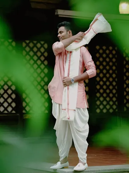 A candid shot of the groom in his traditional South Indian attire, framed by green leaves. This photo captures a natural, unposed moment, showing his happy anticipation.
