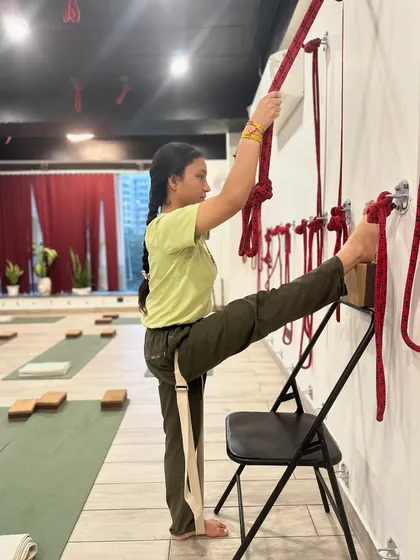 Alignment is everything. Here, a student uses a chair, belt, and wall ropes to practice a standing leg stretch. This setup ensures stability and allows for a safe, deep opening of the hamstrings and hips.
