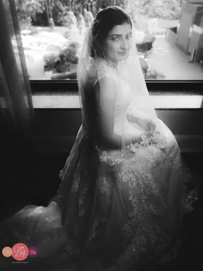 A soft, window-lit portrait of the bride, Shreya, in her white wedding gown, captured in timeless black and white.