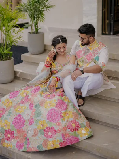 A sweet moment on the steps, the bride adjusting her bangles while the groom looks on with affection.